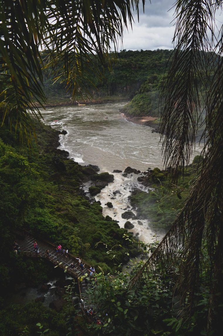 Rio Iguaçu visto por entre a vegetação, com passarela ao fundo
