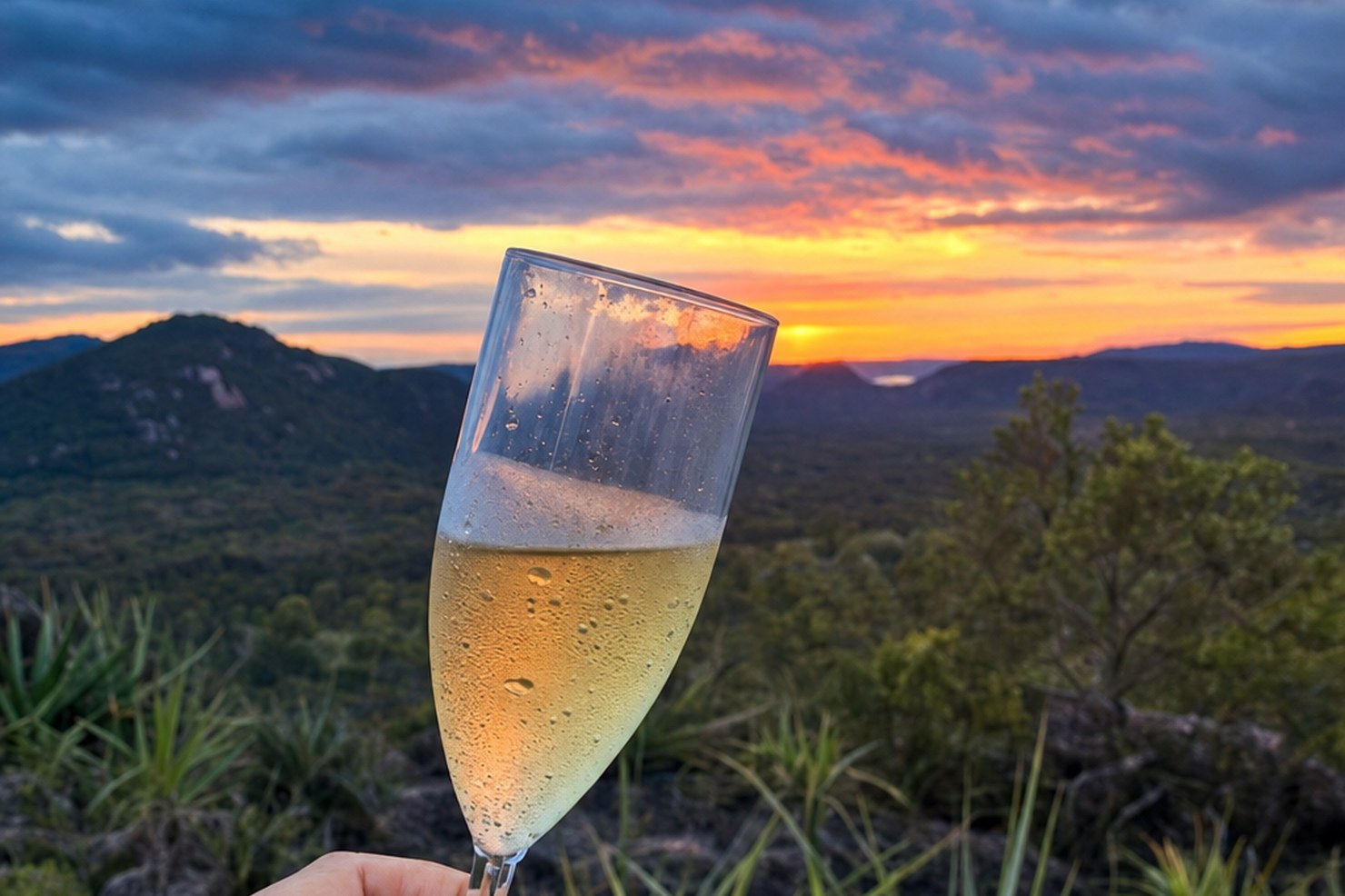 Taça de vinho frisante erguida contra o pôr do sol no cerrado da Chapada das Mesas