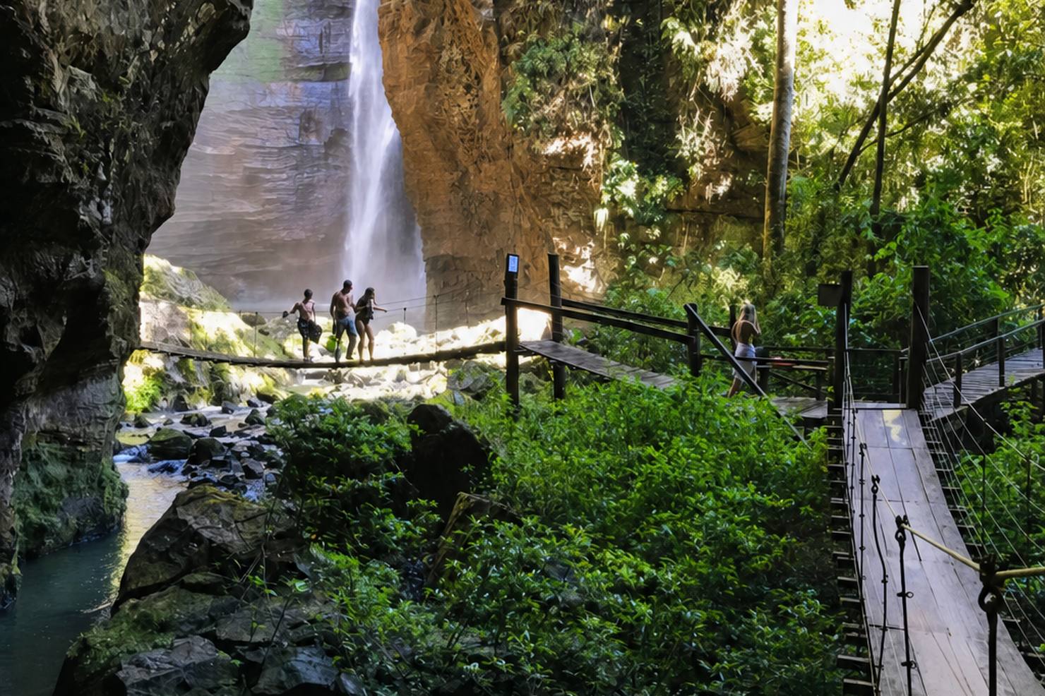 Cachoeira alta em cânion de arenito com passarela suspensa de madeira, no Complexo Pedra Caída