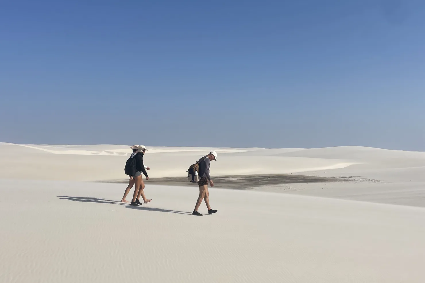 Dois caminhantes com mochilas cruzando o mar de dunas dos Lençóis Maranhenses