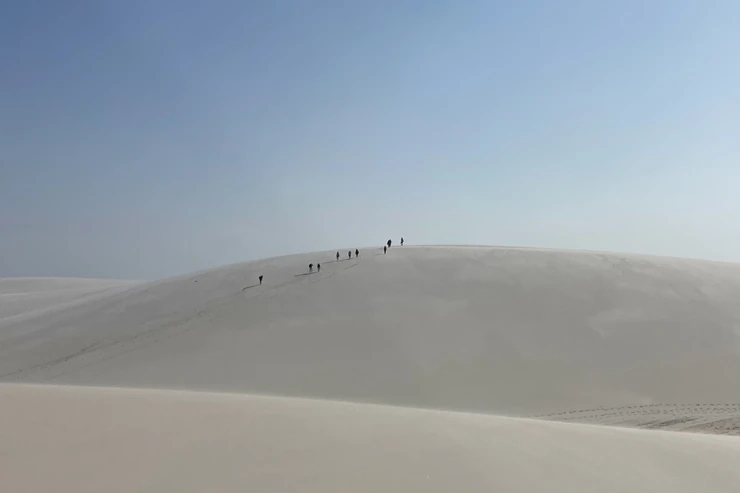 Grupo de caminhantes atravessando a crista de uma duna nos Lençóis Maranhenses