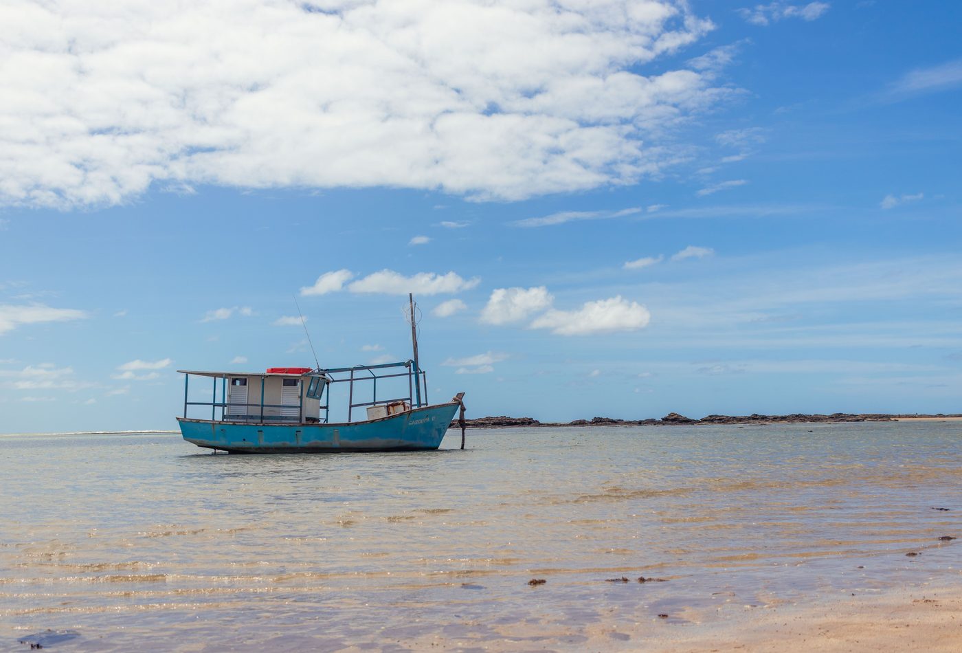 Barco de pesca azul ancorado em água rasa junto ao recife em Morro de São Paulo