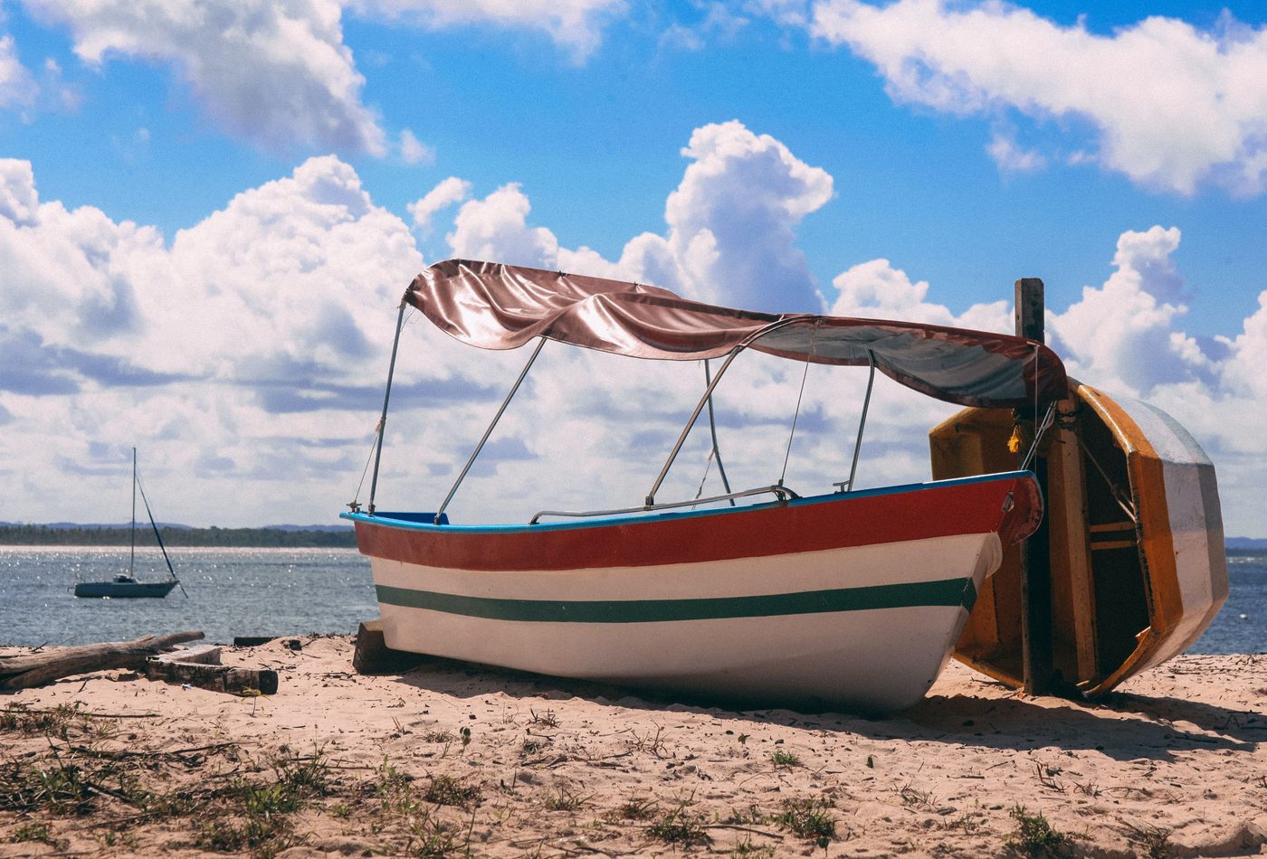 Barco de madeira colorido na areia da praia em Morro de São Paulo, sob céu de nuvens