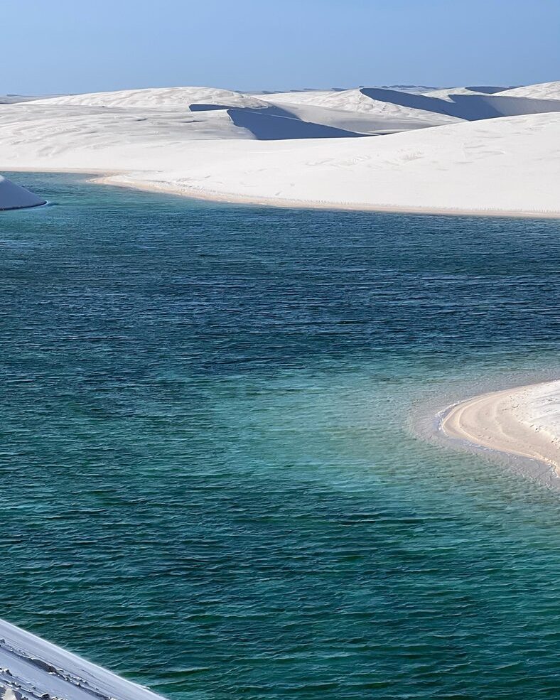 Lagoa de água doce esverdeada ao pé de uma duna branca nos Lençóis Maranhenses