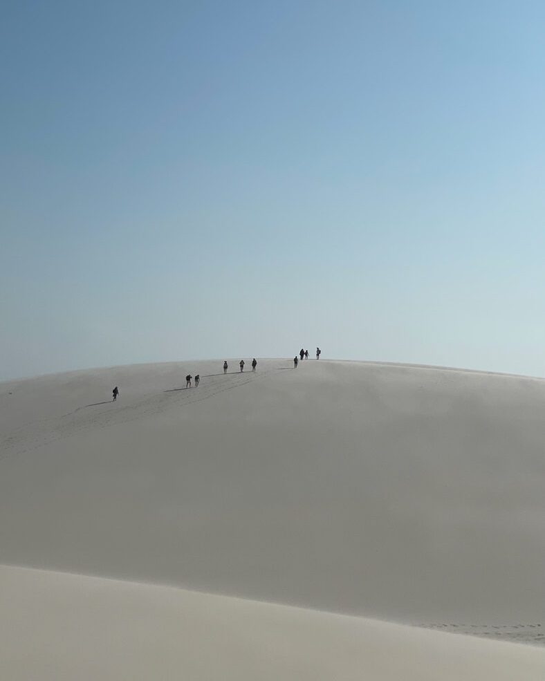 Fila de pessoas ao longe caminhando na crista de uma duna gigante
