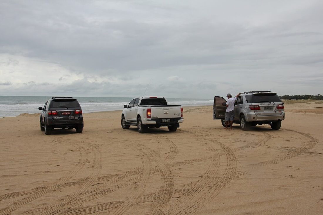 Veículos 4x4 estacionados sobre a areia na entrada do campo de dunas
