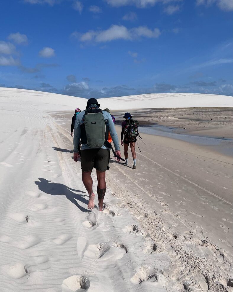 Caminhantes com mochila subindo uma duna durante a travessia a pé dos Lençóis
