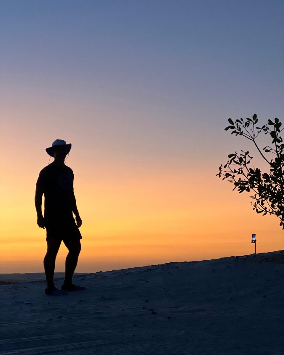 Silhueta de uma pessoa contra o céu alaranjado no fim da tarde