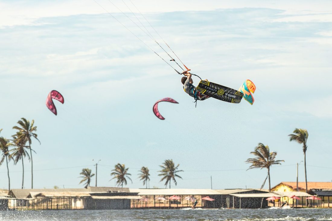 Kitesurfistas com pipas coloridas sobre a praia com coqueiros