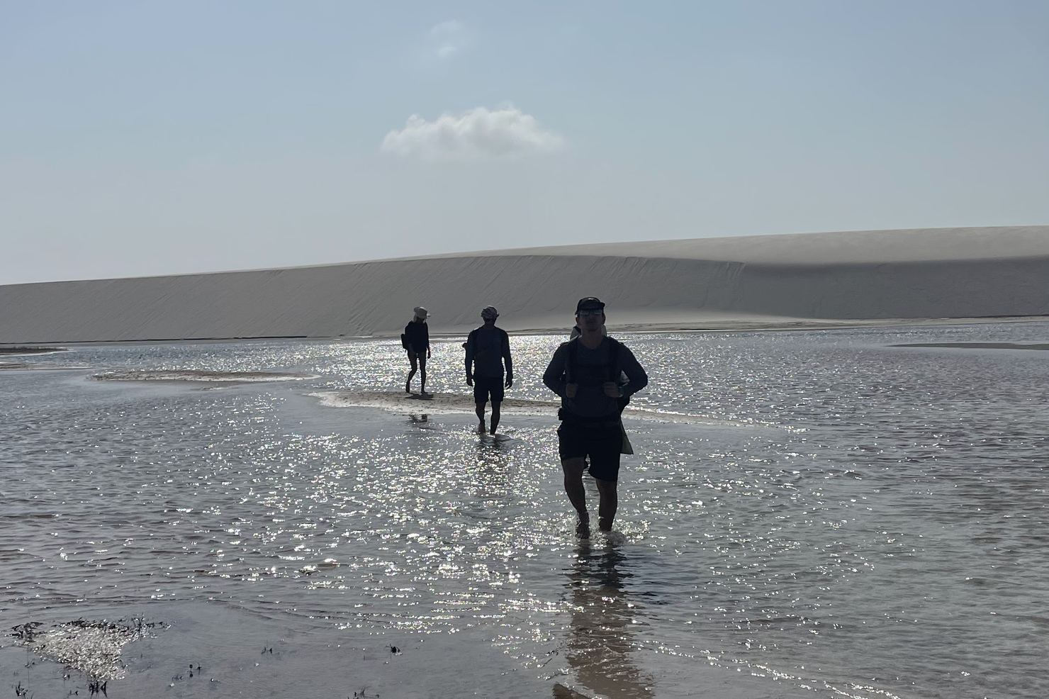 Caminhantes atravessando uma l&acirc;mina de &aacute;gua entre dunas nos Len&ccedil;&oacute;is Maranhenses